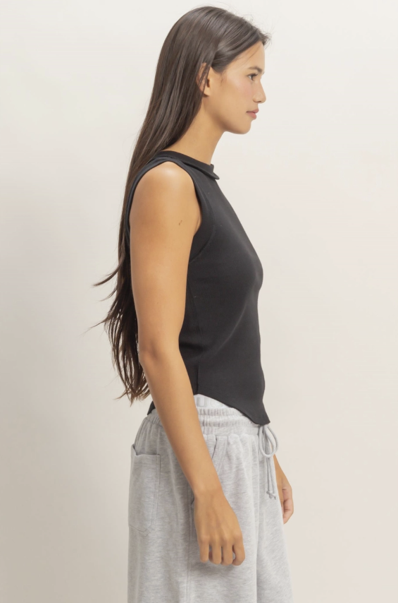 Woman wearing a black sleeveless top and gray pants against a plain background