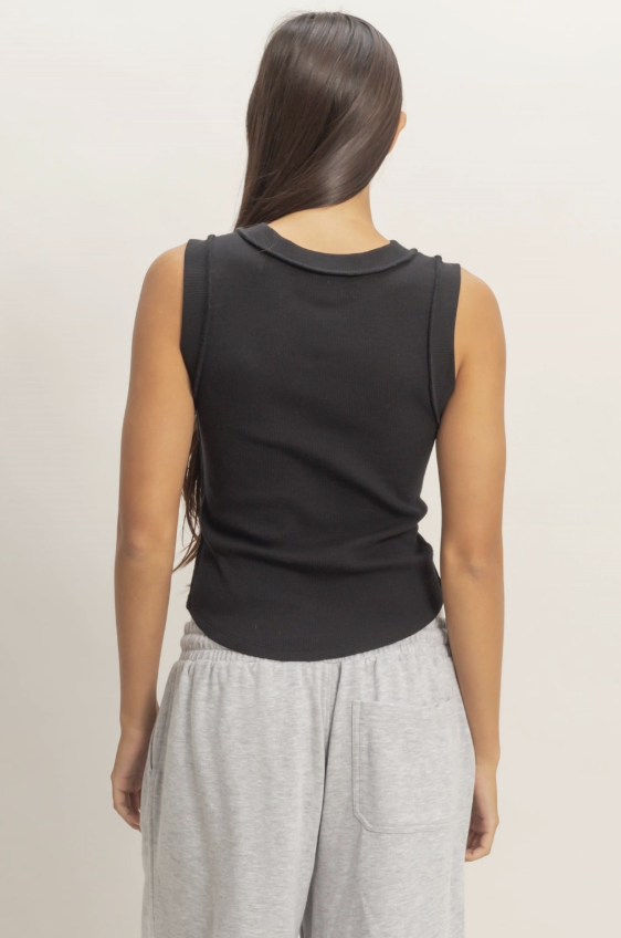 Person wearing a black sleeveless top and gray pants on a plain background