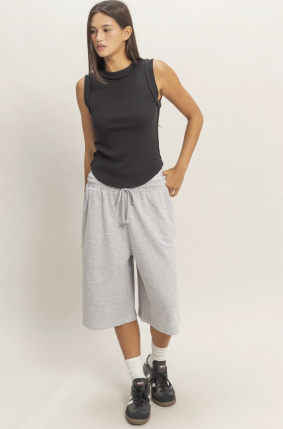 Woman wearing a black sleeveless top and gray wide-leg pants on a white background