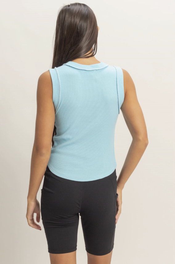 Woman wearing a light blue sleeveless top and black shorts on a beige background