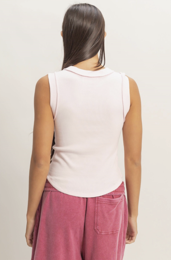 Person wearing a white sleeveless top and pink pants against a plain background