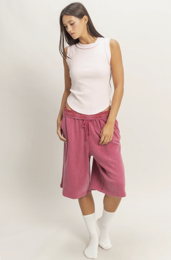 Woman wearing a white sleeveless top and pink shorts on a plain background