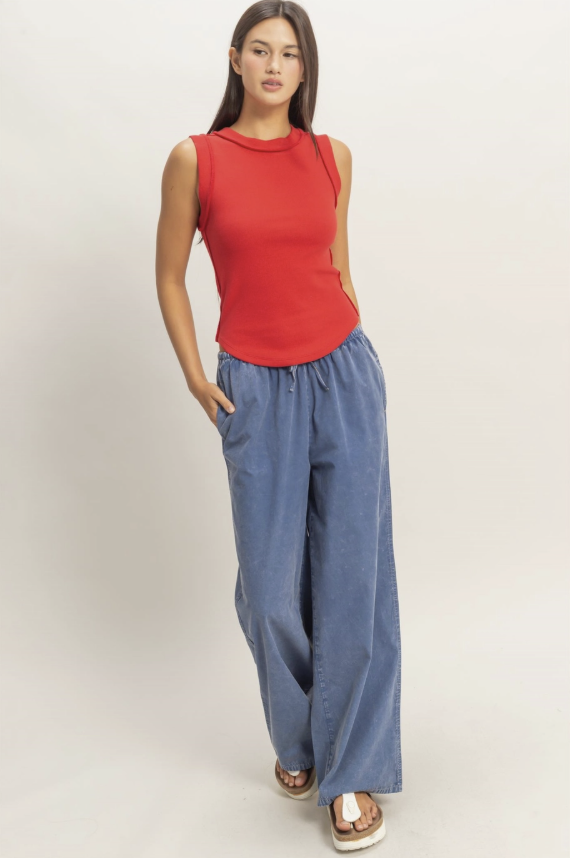 Woman wearing a red sleeveless top and blue wide-leg pants on a plain background