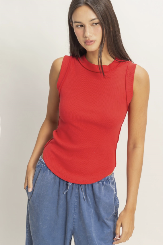 Woman wearing a red sleeveless top and blue pants on a plain background