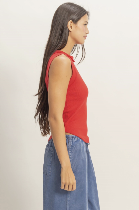 Woman wearing a red sleeveless top and blue jeans on a plain background