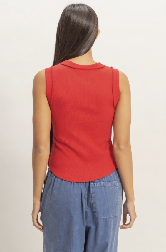 Person wearing a red sleeveless top and blue pants on a plain background