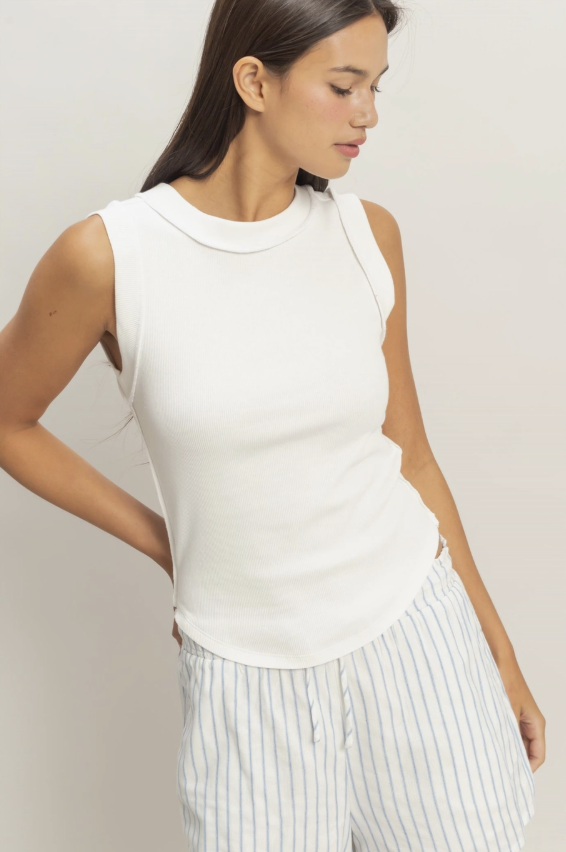 Woman wearing a white sleeveless top and striped pants against a plain background