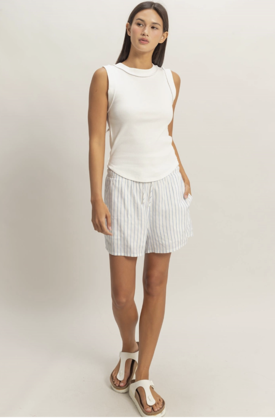 Woman wearing a white sleeveless top and striped shorts on a plain background