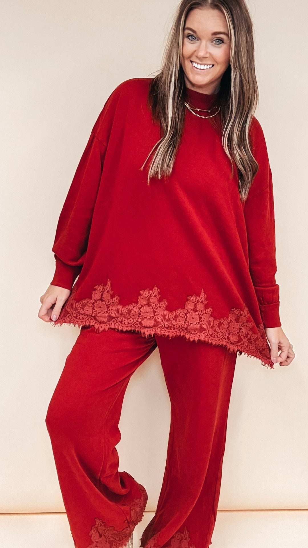 Woman wearing burgundy matching set with lace trim at ankles and bottom of shirt on plain background