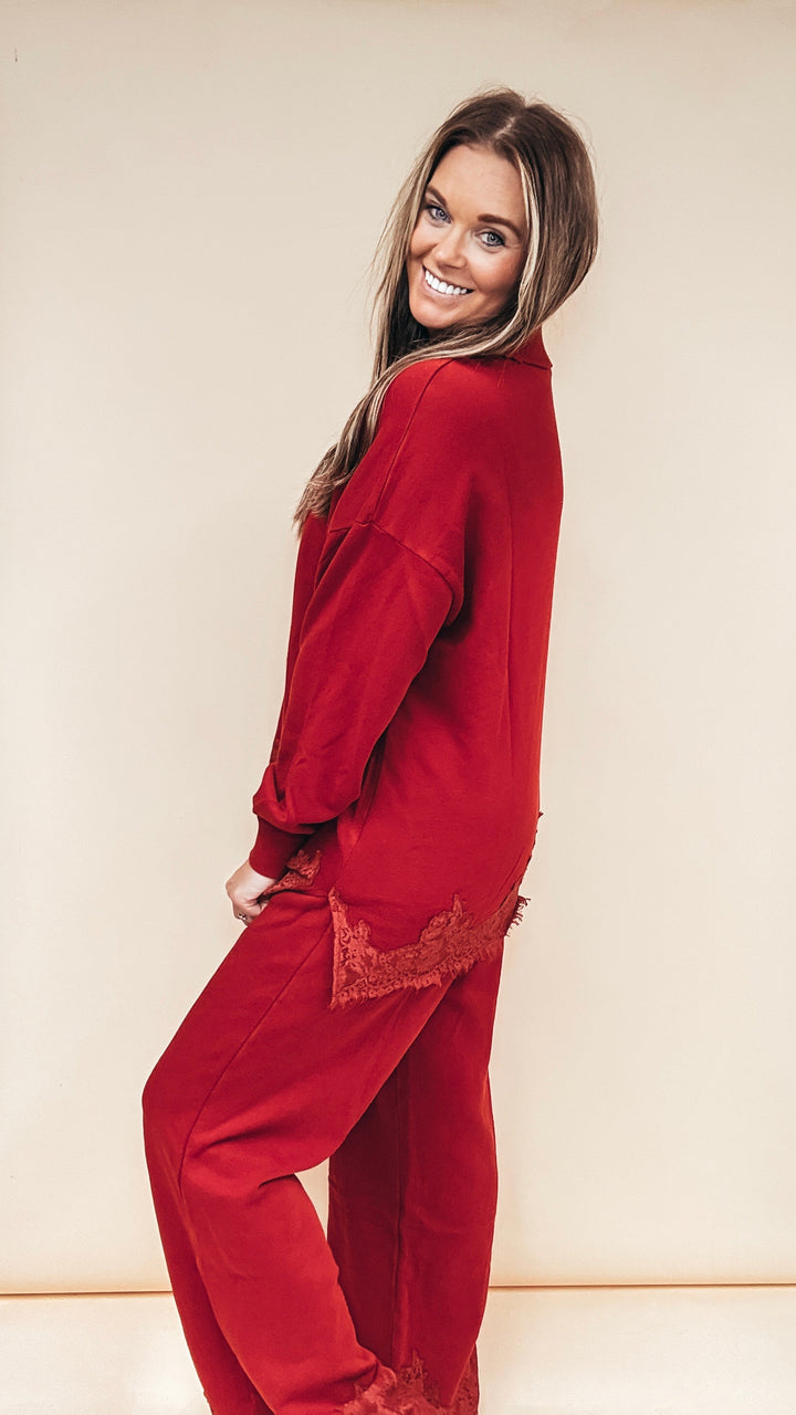 A woman modeling a matching red lounge set consisting of a long-sleeve top and wide-leg pants, standing against a plain beige studio background.