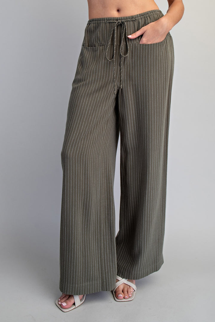 Person wearing olive green striped wide-leg pants on a gray background