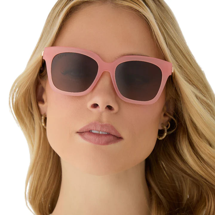 Woman wearing pink sunglasses with a plain background