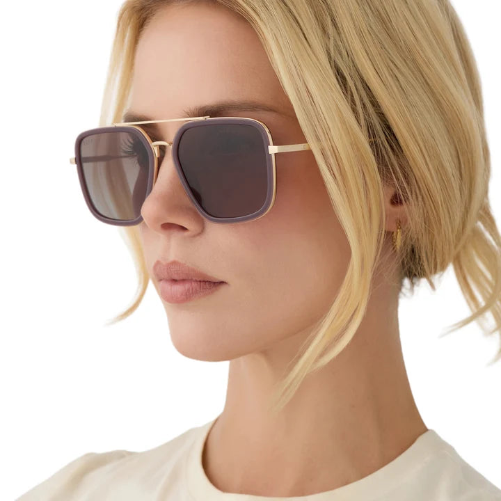 A close-up side profile of a blonde woman wearing oversized square sunglasses with dark tinted lenses and thin gold metal frames.