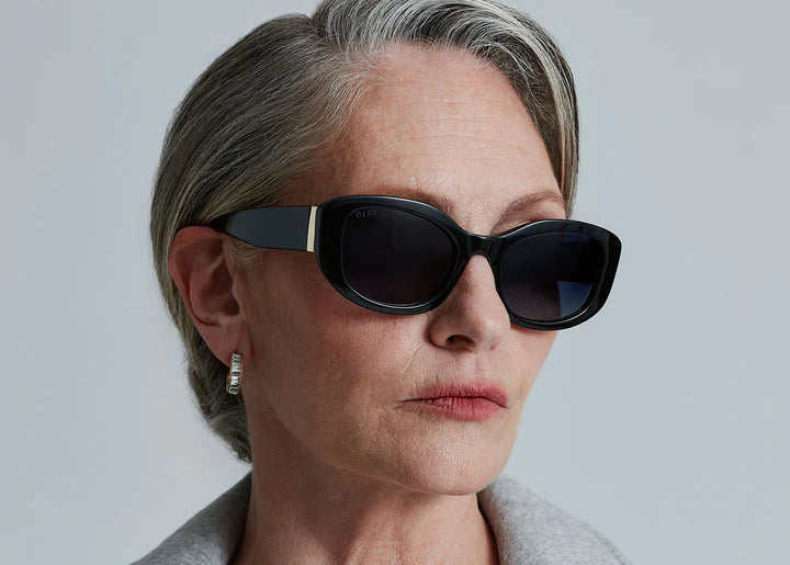 Woman wearing black sunglasses with gold detail on plain background