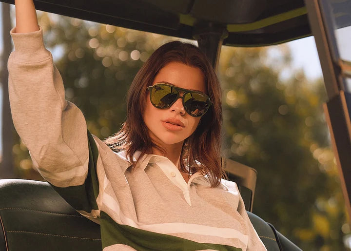 Woman in golf card wearing stripe top and green sunglasses outdoors