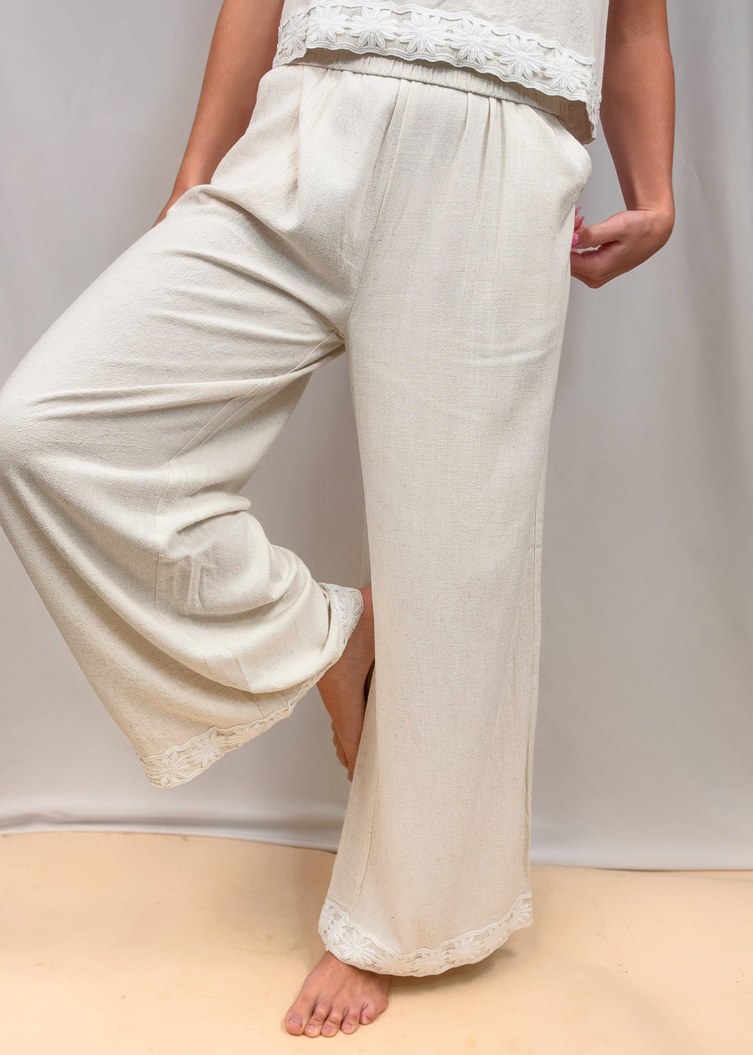 Woman wearing matching linen set with floral design on ankles and waist on plain background