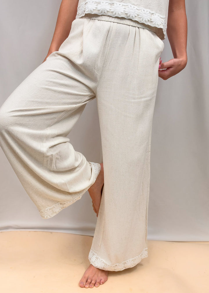 Woman wearing matching linen set with floral design on ankles and waist on plain background