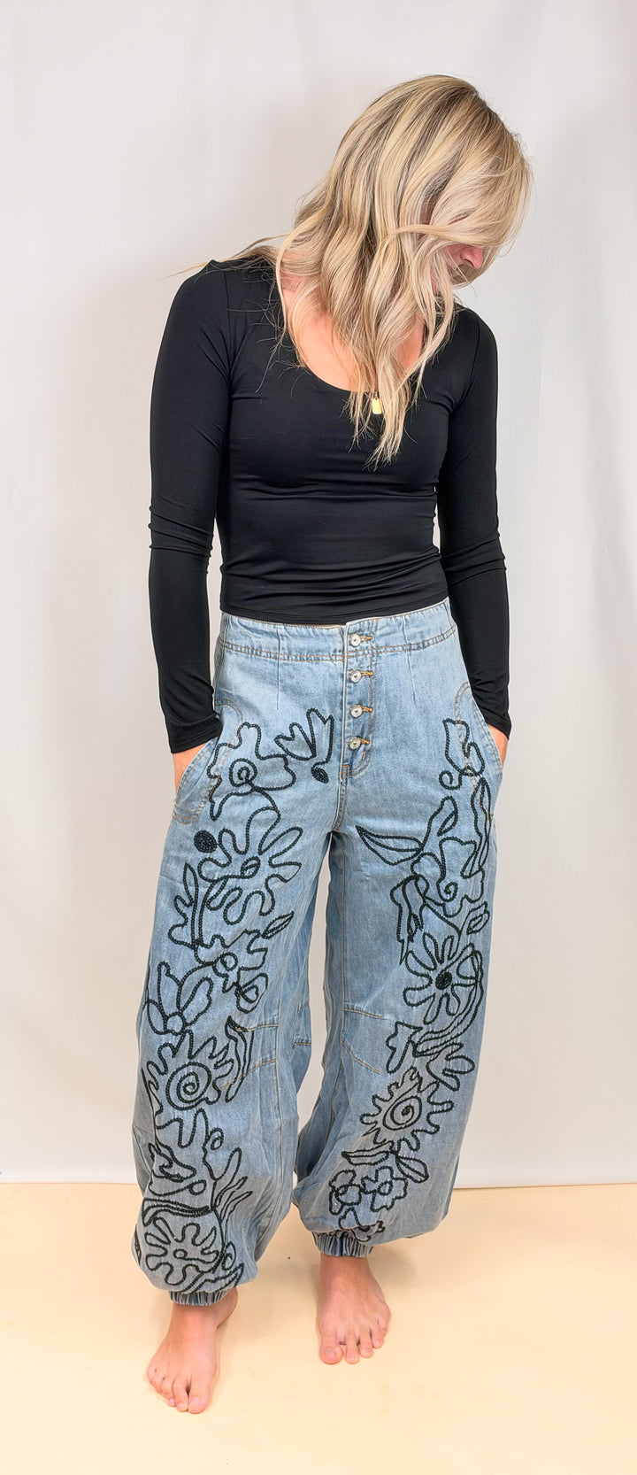 Woman wearing black shirt with denim jeans with floral embroidery on plain background