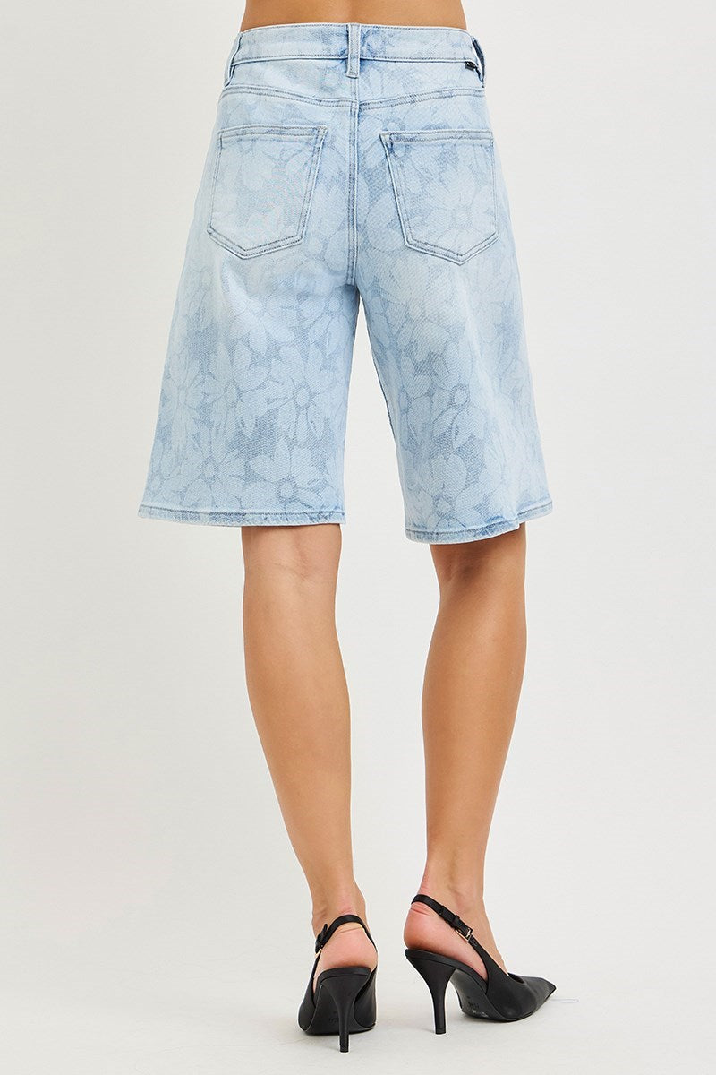 woman wearing denim bermuda shorts with floral pattern on plain background