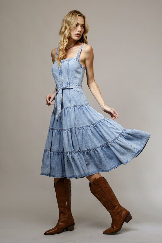 Woman wearing a denim dress and brown knee-high boots on a plain background