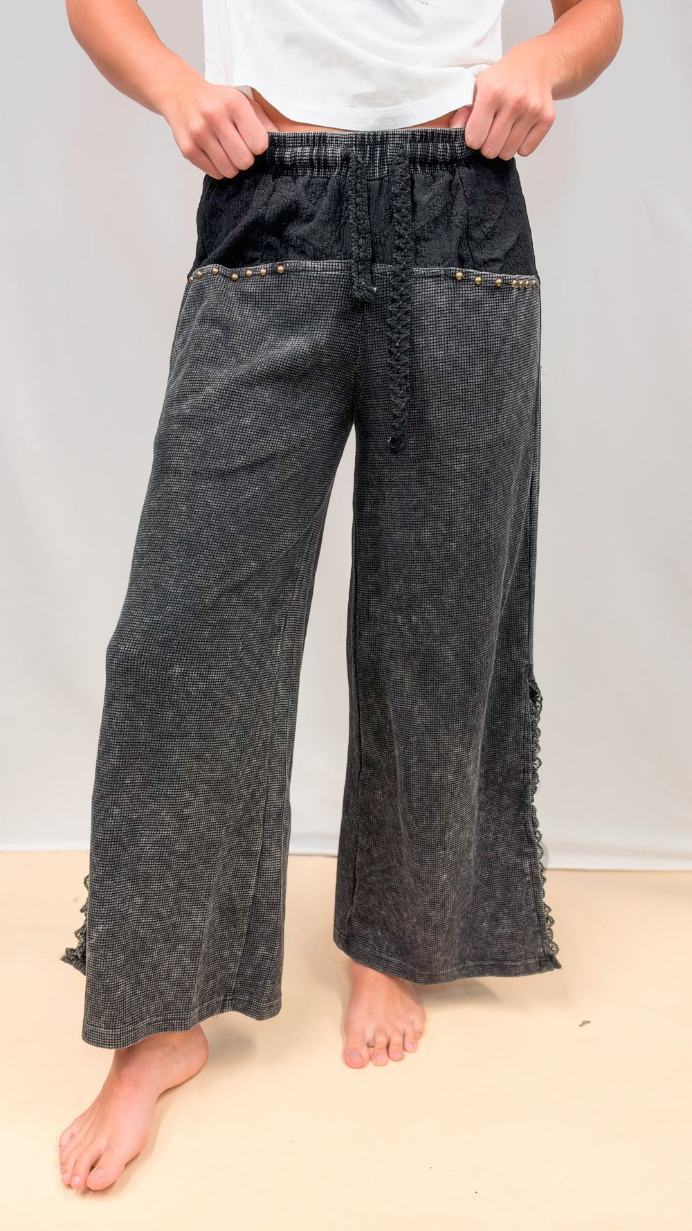 Woman wearing black waffle knit pants with lace details on plain background