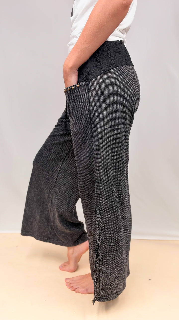 Woman shown from side view wearing black waffle knit pants and white top on plain background