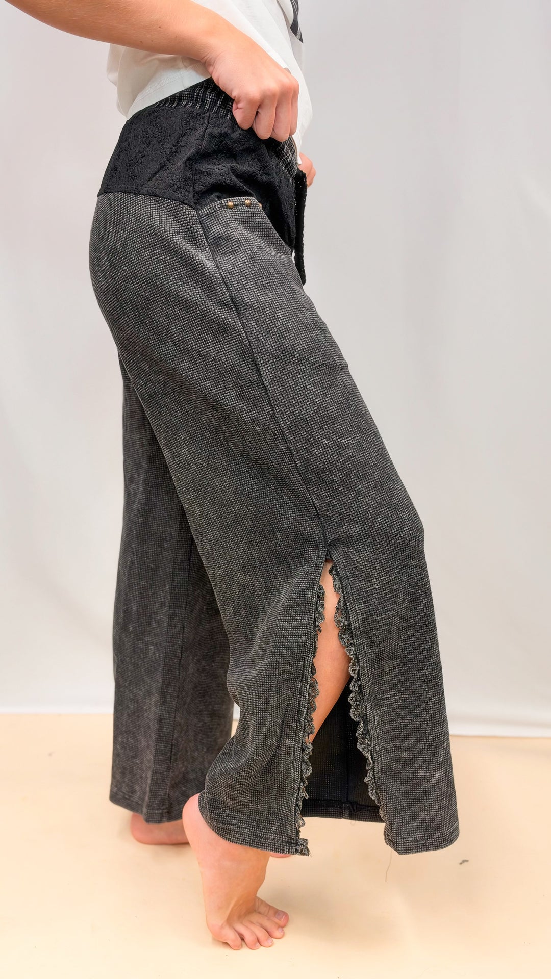 Woman shown from side view wearing black waffle knit pants with lace detail on plain background