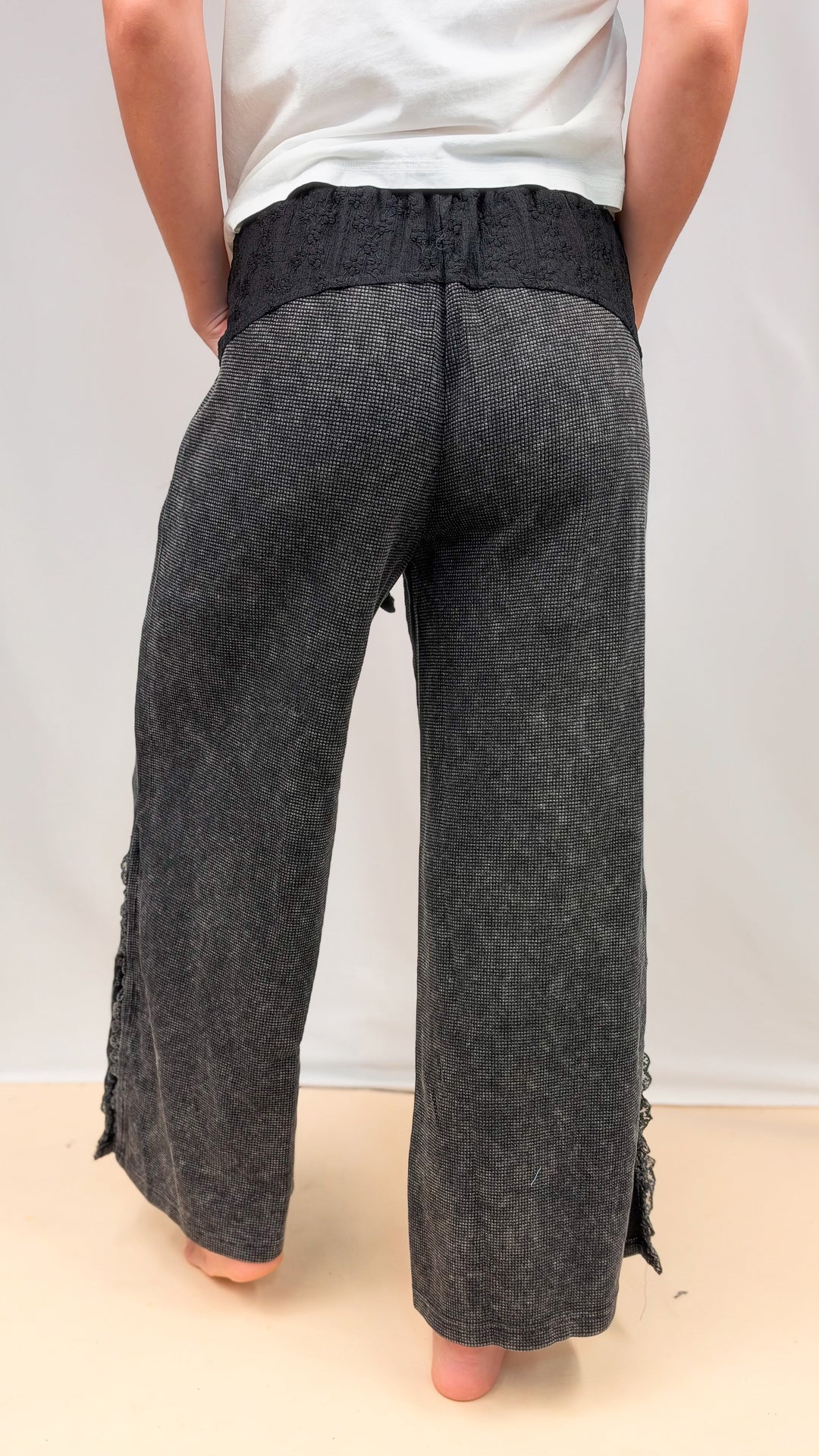 Woman shown from back view wearing black waffle knit pants with lace detail on plain background