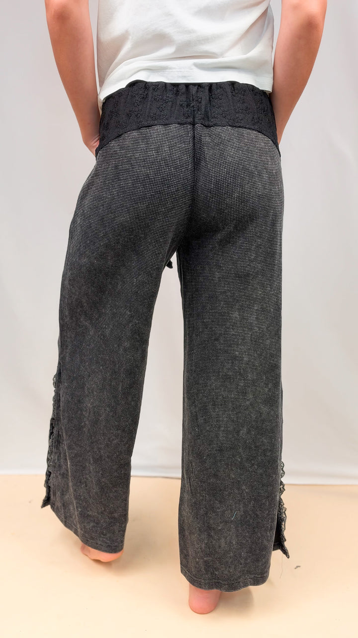 Woman shown from back view wearing black waffle knit pants with lace detail on plain background