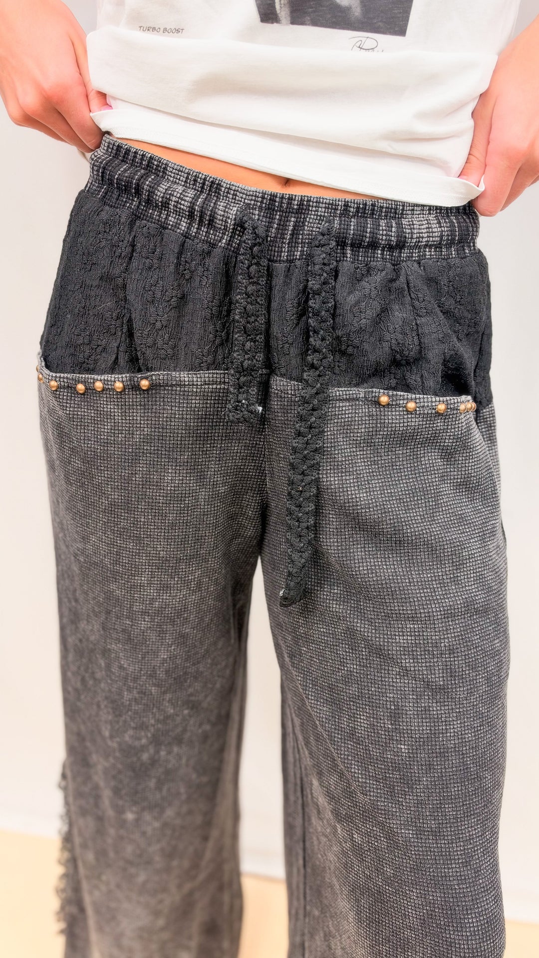 Close up of woman wearing black waffle knit pants with lace detail on plain background