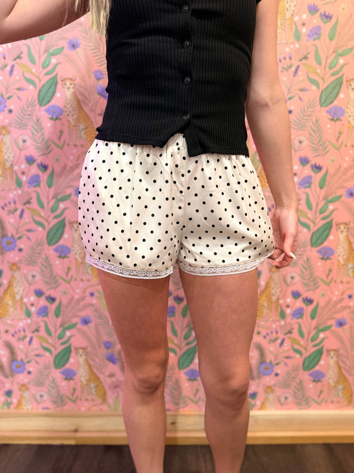 Person wearing polka dot shorts and a black top against a pink floral background