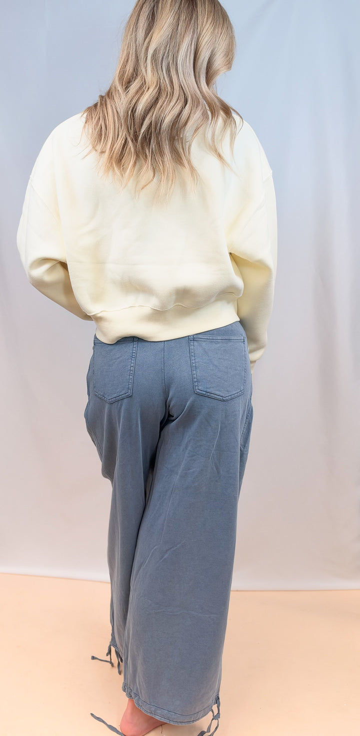woman shown from back view wearing cream cropped sweatshirt with blue pants on plain background