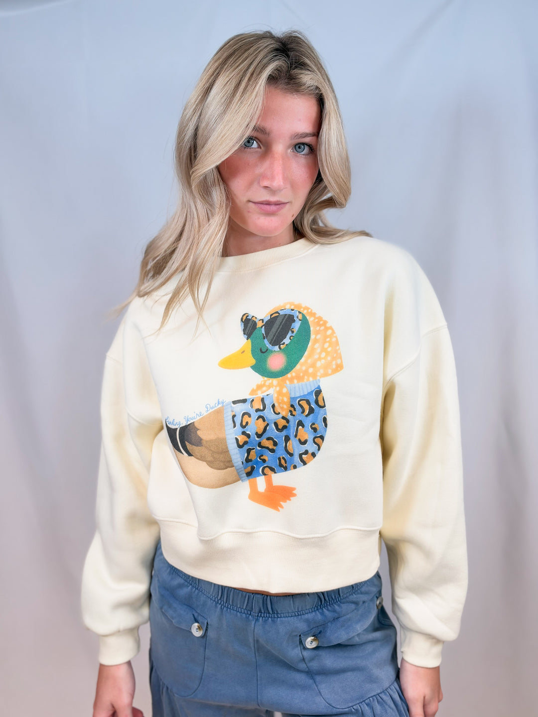 Woman wearing cream cropped sweatshirt with duck graphic on plain background