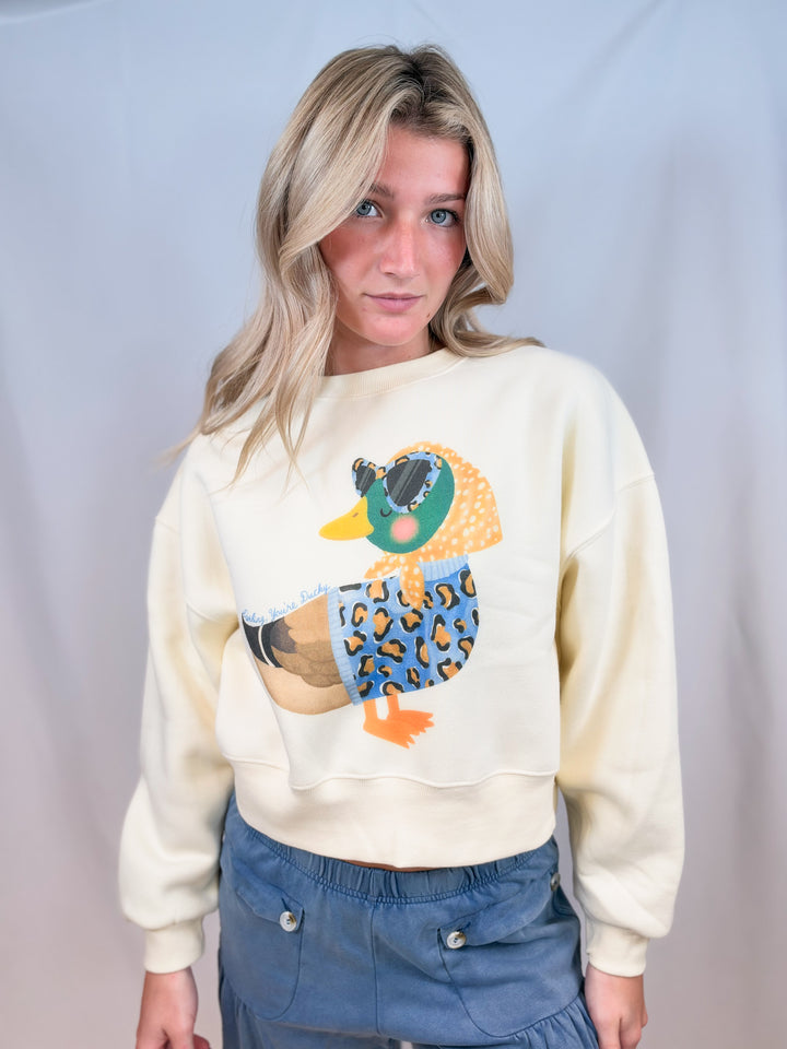 Woman wearing cream cropped sweatshirt with duck graphic on plain background