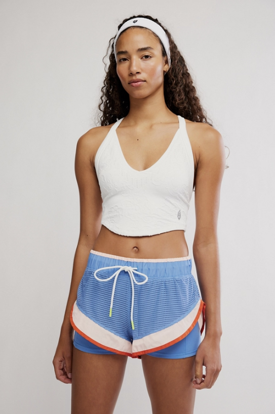 Woman wearing a white tank top and blue shorts with a colorful trim on a plain background