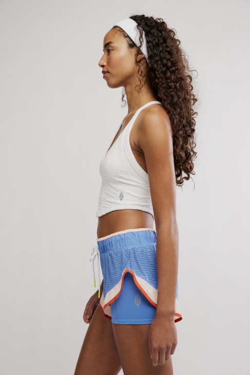 Woman wearing a white sports bra and blue shorts with a colorful trim on a plain background
