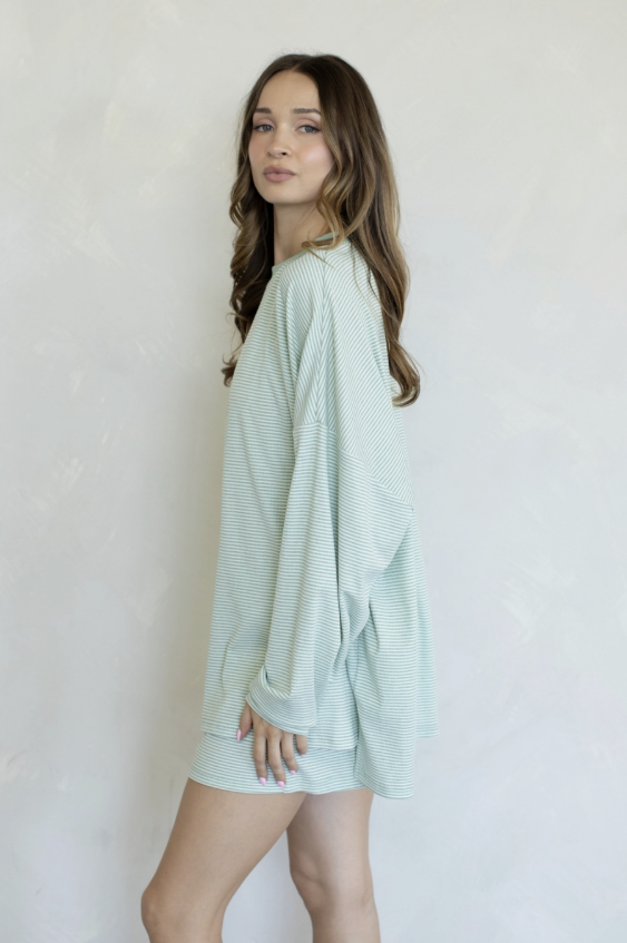 A woman modeling a light mint green waffle-knit long-sleeve tunic top or mini dress against a textured off-white wall.
