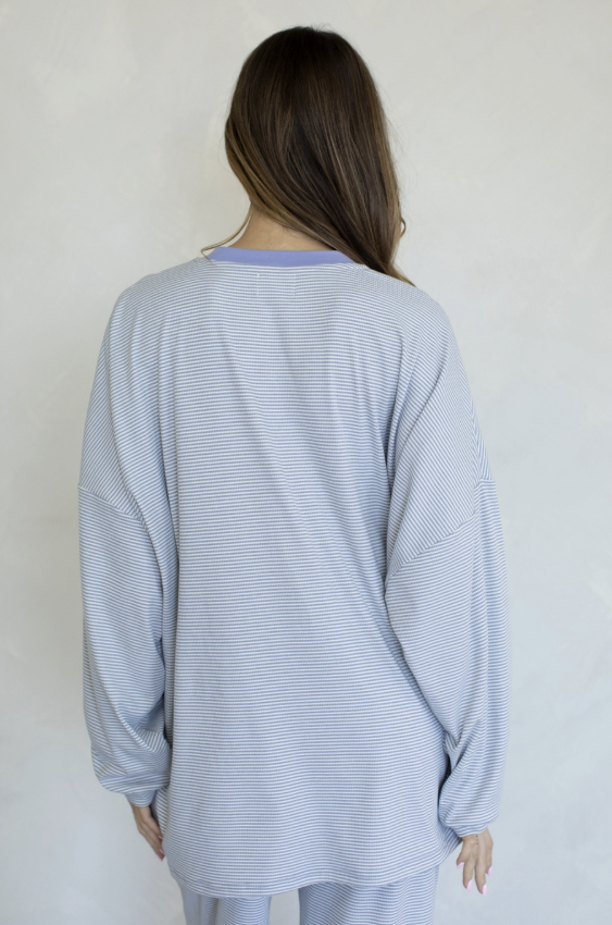 A woman viewed from behind wearing a light blue and white striped long-sleeve top and matching pants against a plain off-white wall.