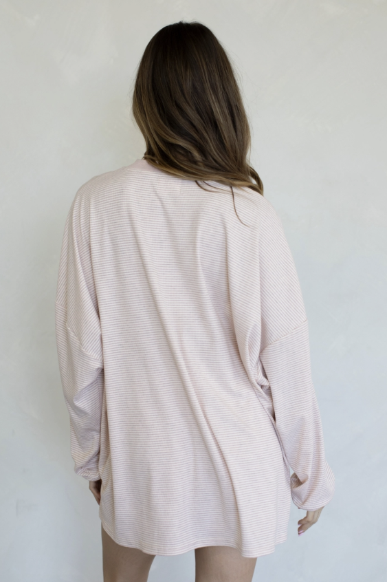 A woman viewed from behind wearing a light pink ribbed long-sleeve top against a plain light gray wall.
