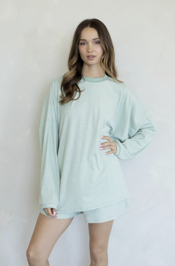 A woman modeling a light mint green long-sleeve top and matching shorts set against a textured off-white wall.
