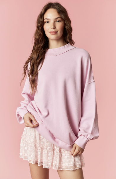 Woman wearing a pink oversized sweater over a lace dress on a pink background