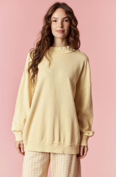 Woman wearing a light yellow sweatshirt and pants against a pink background