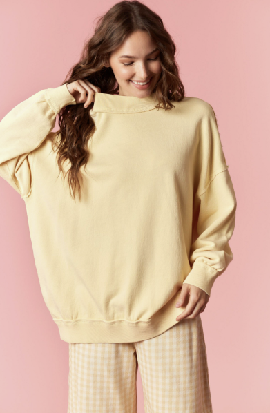 Woman wearing a light yellow sweatshirt against a pink background