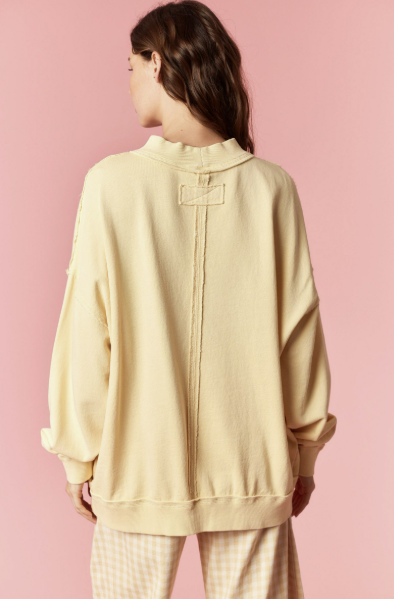 Person wearing a light yellow oversized sweatshirt and pants on a pink background