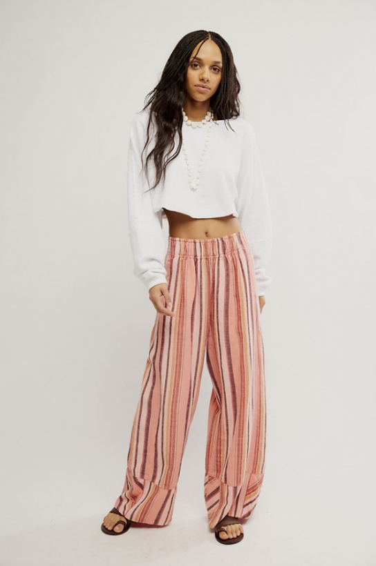 Woman wearing a white cropped top and pink striped pants on a plain background