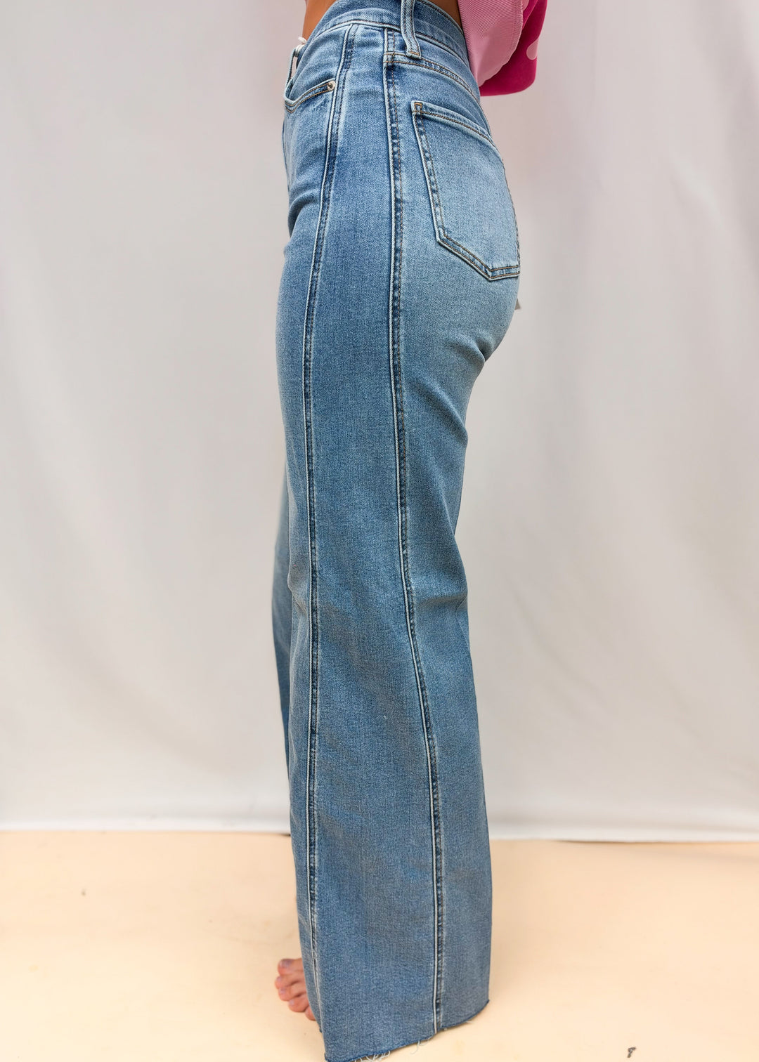 Woman shown from side wearing medium wash wide leg denim jeans with side seaming detail on plain background