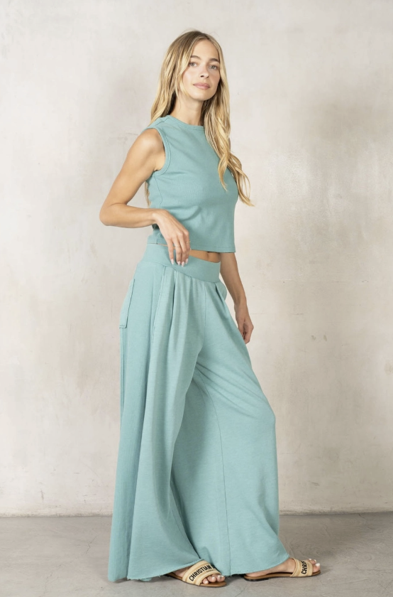 Woman wearing a light blue sleeveless top and wide-leg pants against a neutral background
