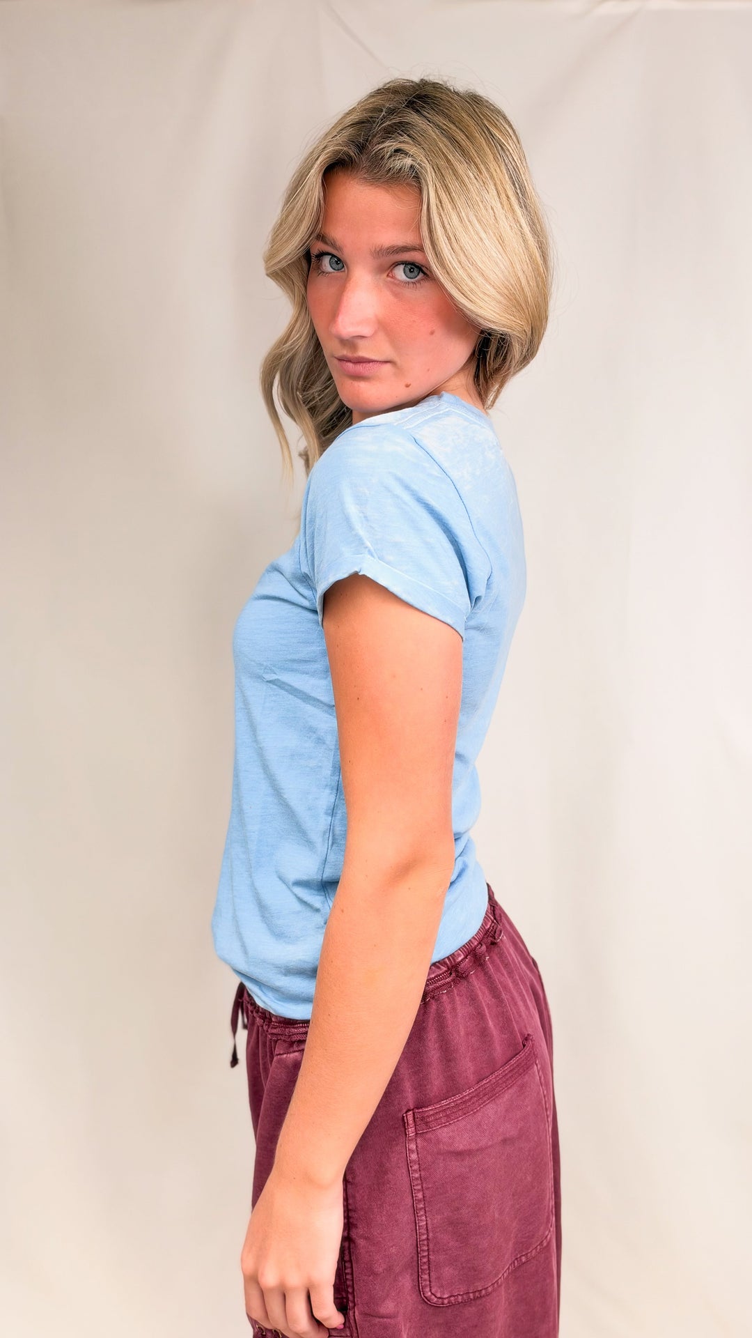 Woman wearing blue tee with maroon pants on plain background