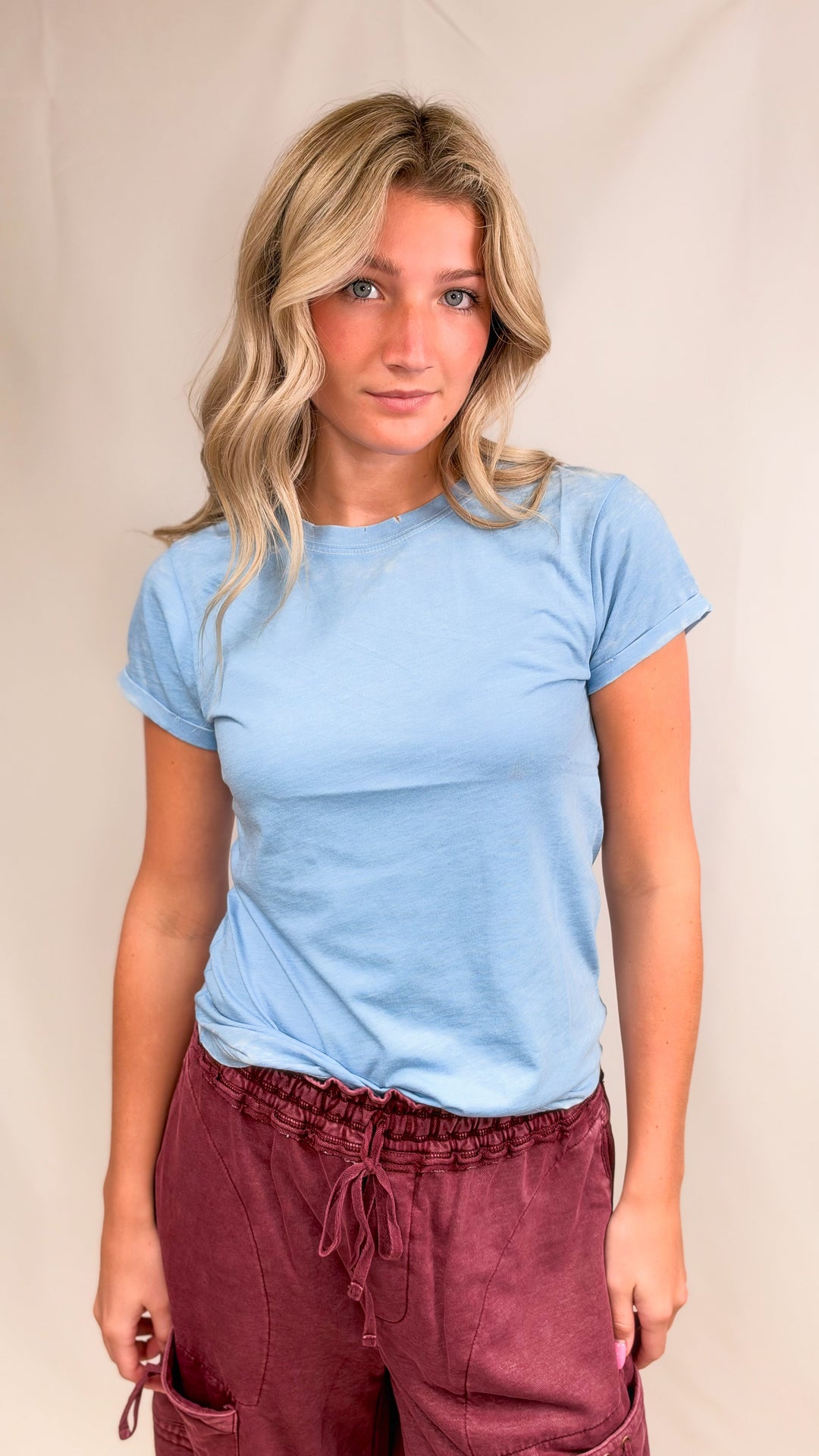 Woman wearing blue tee with maroon pants on plain background