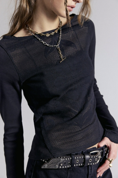 A close-up of a model wearing a black textured knit long-sleeve top with a wide boat neckline, layered with gold chain necklaces, paired with a black studded belt.